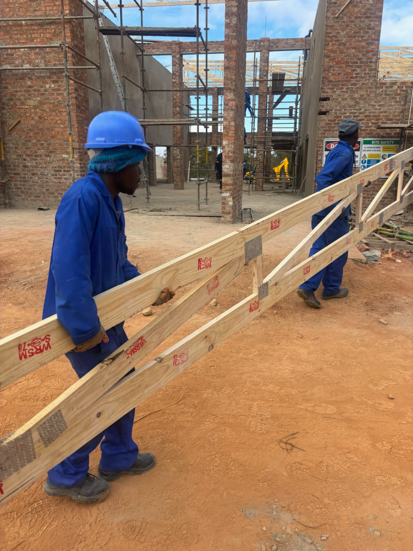 Site team carrying a timber roof truss across a construction site