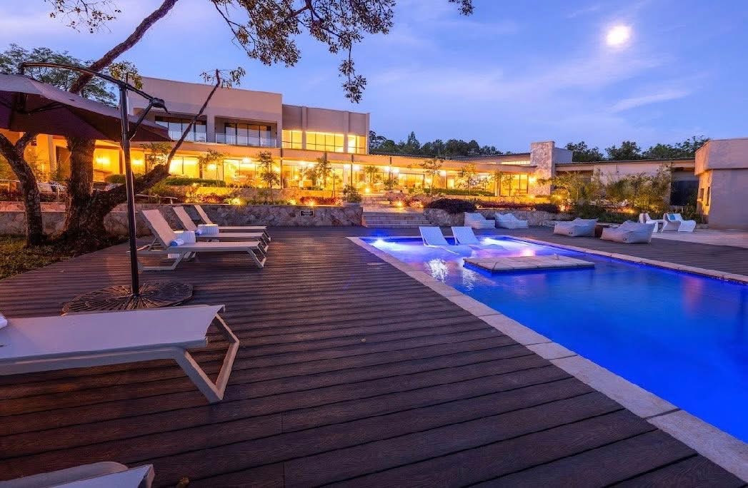Illuminated swimming pool and timber deck with sun loungers at White River Manor at dusk