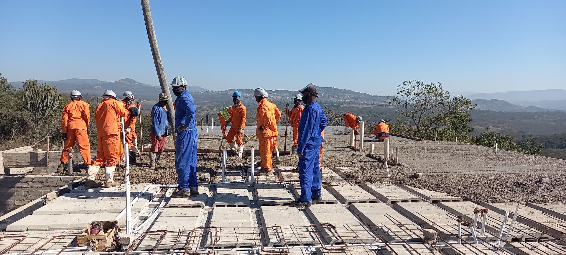 Workers finishing a rib-and-block slab with valley views behind
