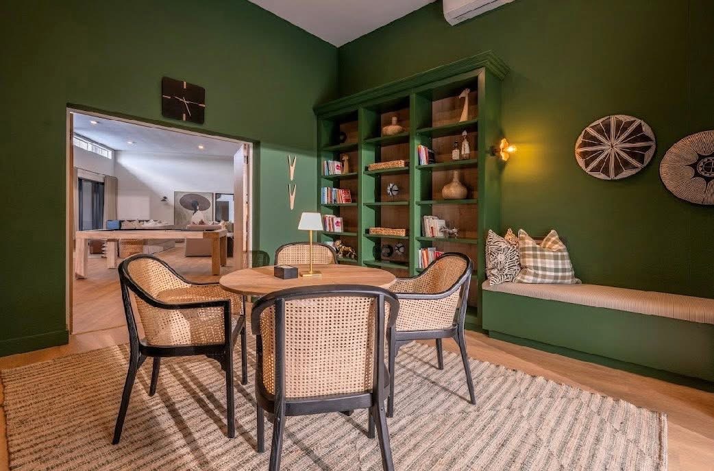 Snug lounge at White River Manor with a round wooden table, cane chairs and a built-in green bookcase