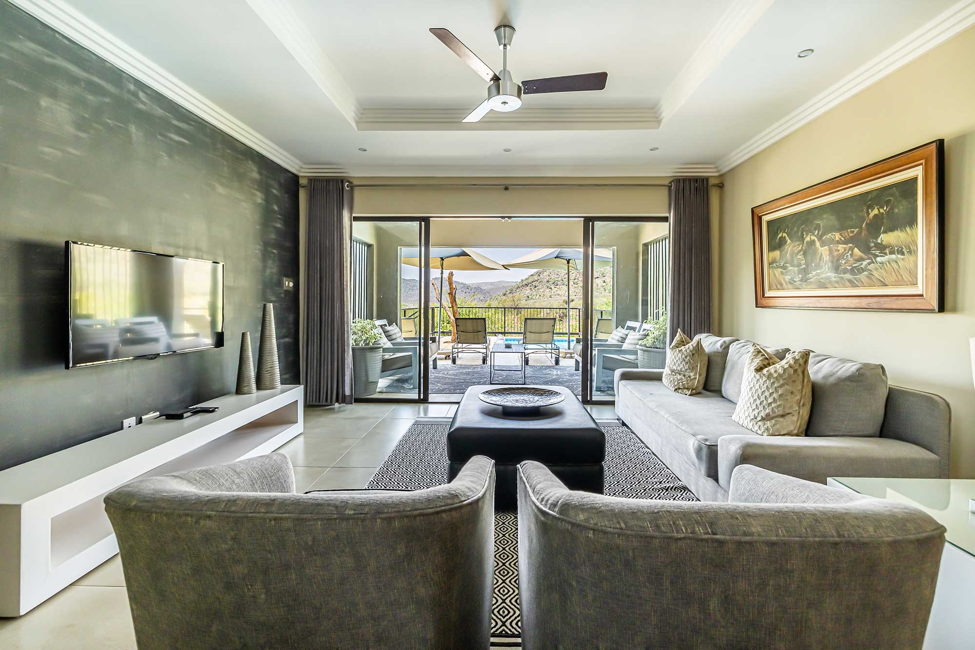 Lodge lounge with sofas and a central ottoman leading through sliding glass doors to a covered patio, swimming pool and mountains beyond